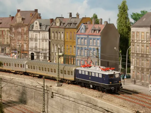 Blaue Ellok mit Personenzug vor Altbauten